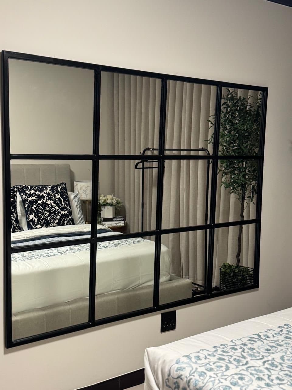Large black grid wall mirror reflecting a bedroom
